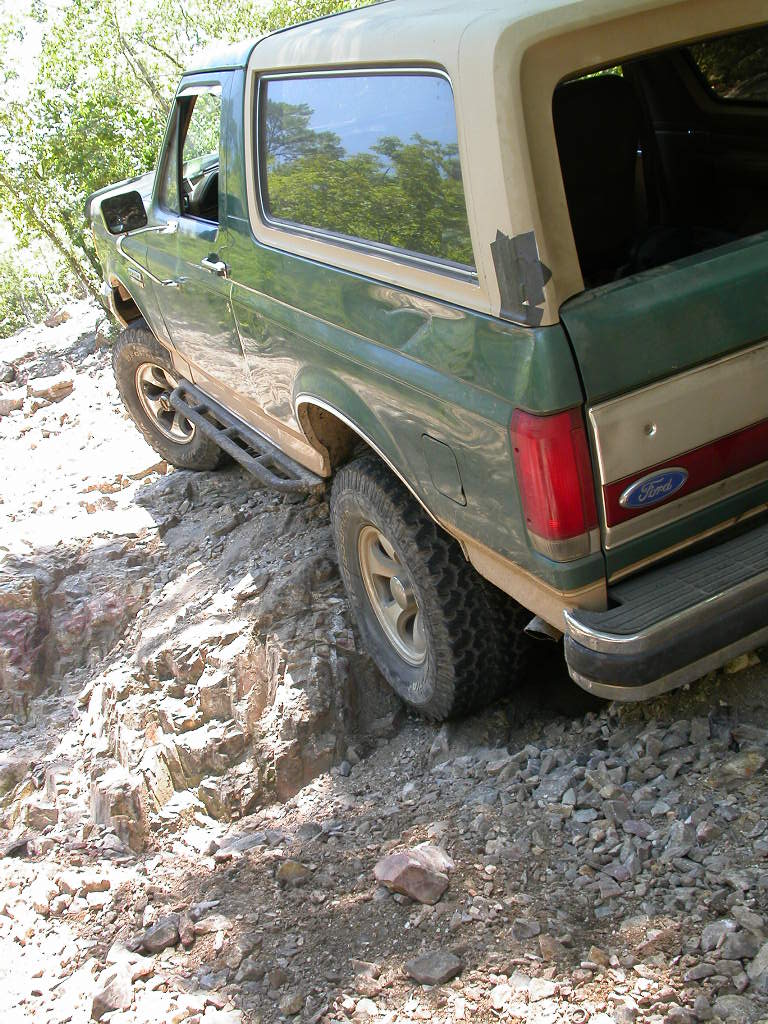 Green Ford Bronco driving on a rocky trail, tires on rocks