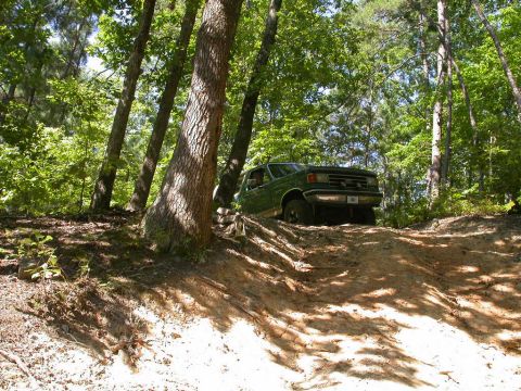 1990 Ford Bronco - A green Ford Bronco navigates a steep, sandy trail through a dense forest.