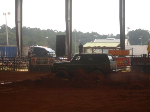 1989 Ford Bronco - A 1989 Ford Bronco navigates a muddy track, with a truck displaying "WELCOME RACE FANS" in the background.