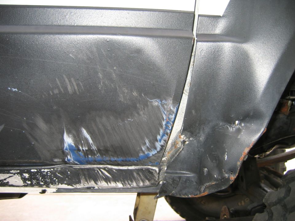 Bedliner-coated truck door and quarter panel with body filler at a sanded dent repair