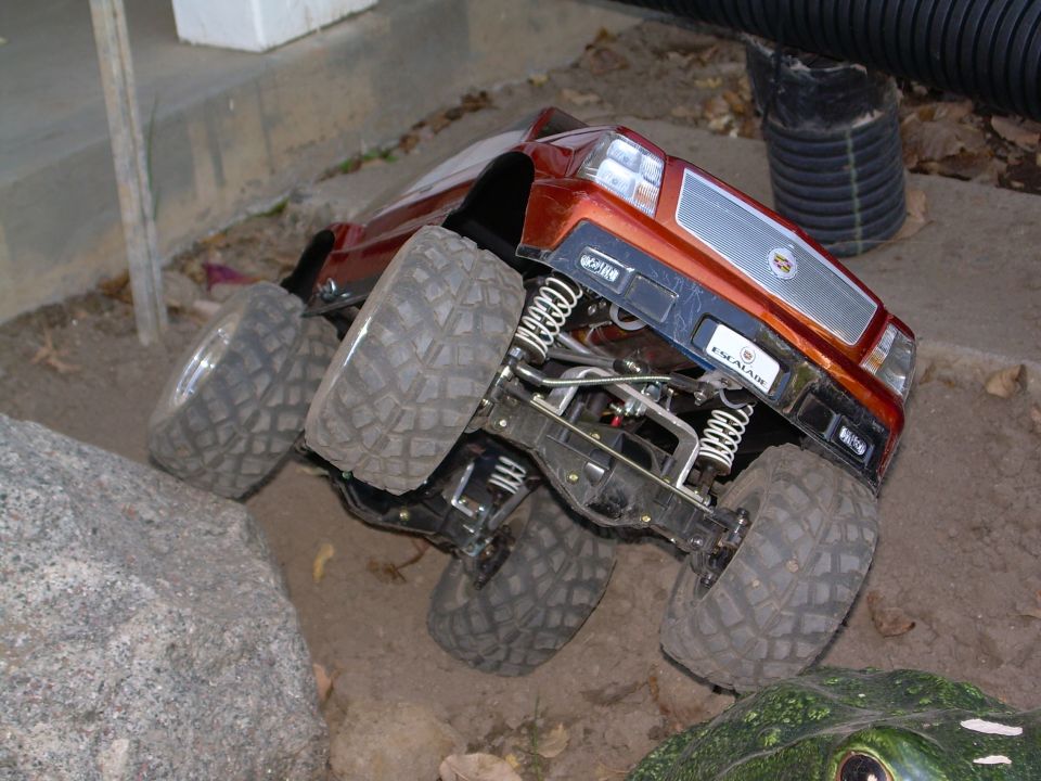 Rear underside of orange Escalade RC crawler in dirt showing axle, links and drag tires