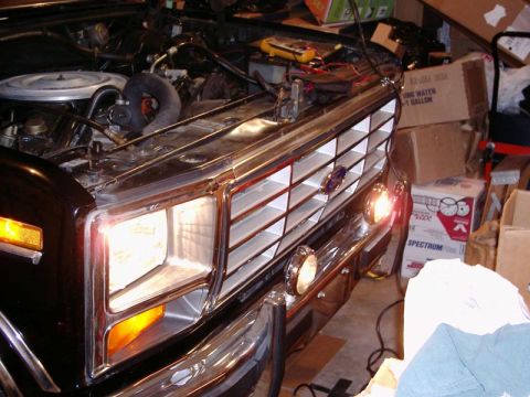 1984 Ford Bronco - The front end of a 1980s Ford Bronco is visible, with its grille and headlights illuminated, suggesting work is being done on the vehicle.
