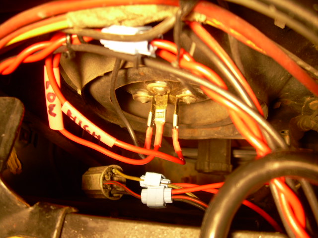 Close-up of a vehicle's headlight wiring harness with red and yellow wires, connectors, and tape labels reading "LOW" and "HIGH"