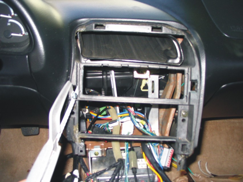 Car dashboard with radio removed, exposing wiring and ductwork in center console.