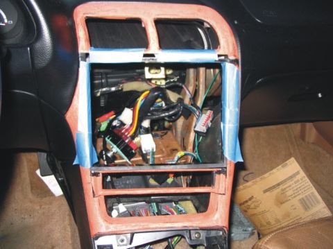 1993 Ford Probe - Interior center console/dash removed on a vehicle, revealing a bundle of wiring harnesses with colored connectors behind the reddish-brown…