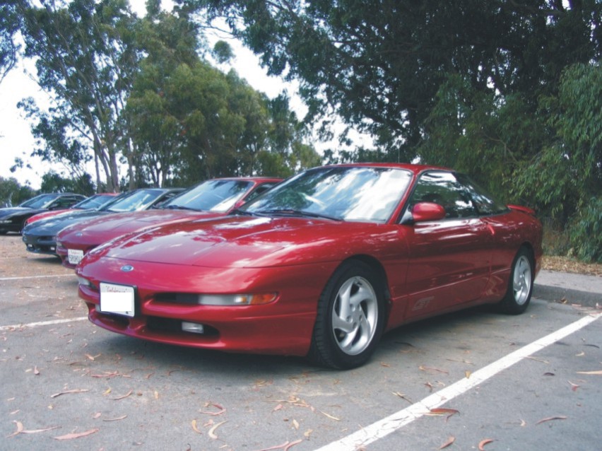 Red Ford Probe GT coupe parked front three-quarter in a lot with trees and other cars behind