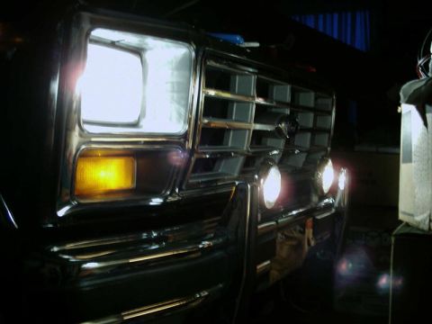 1984 Ford Bronco - Close-up of a vintage Ford truck's front end, highlighting the grille and illuminated headlights.