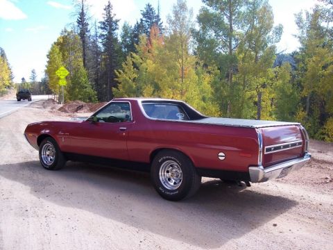 1972 Ford Ranchero - A red 1972 Ford Ranchero pickup truck is parked on a dirt road, with trees displaying autumn colors.