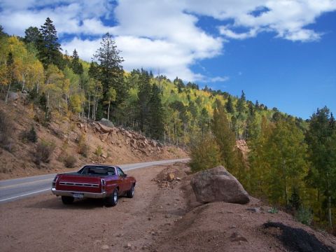 1972 Ford Ranchero - A red pickup truck is parked on the side of a road with a scenic view of a forest in the fall.