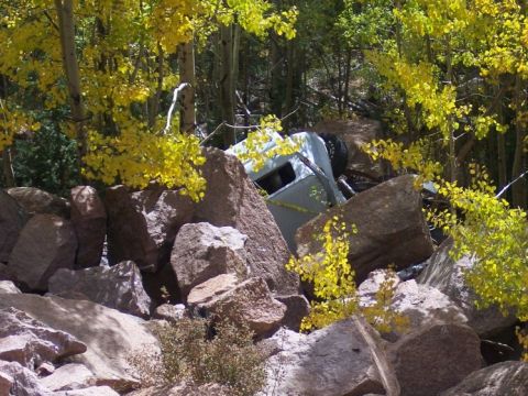 1972 Ford Ranchero - A damaged pickup truck lies on its side, partially obscured by rocks and autumn foliage.
