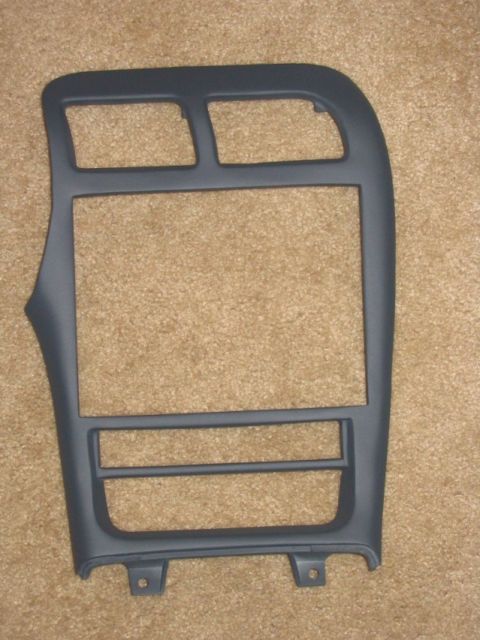 1993 Ford Probe - A gray plastic dashboard center console trim bezel lying on beige carpet, featuring cutouts for a radio/climate stack and dual air vents at…