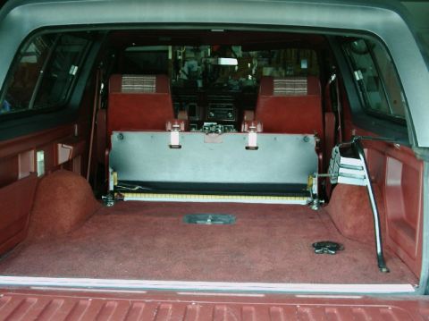 1984 Ford Bronco - The cargo area of an SUV is shown, red carpeting and a metal divider installed behind the front seats.