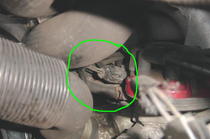 close-up of a gray electrical connector with wires, circled in green, among engine components