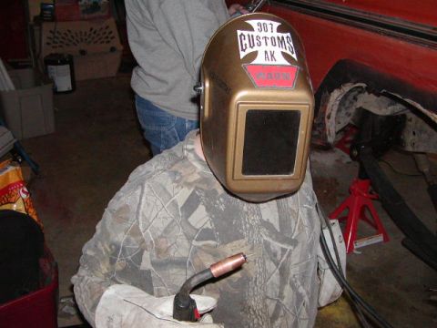 1978 Ford Bronco - A person prepares to weld in a garage, with a vehicle undergoing repairs in the background.