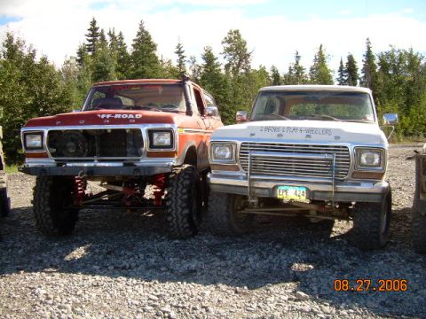 1978 Ford Bronco - Two modified Ford trucks, a Bronco and an F-Series, are parked outdoors with trees behind them.