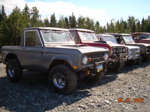 1978 Ford Bronco - A row of Ford Broncos are parked outdoors on a gravel lot with trees in the background.