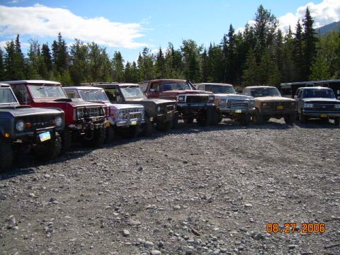 1978 Ford Bronco - A row of 1978 Ford Broncos are parked on a gravel lot with trees and mountains in the background.