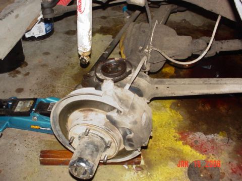 1978 Ford Bronco - Close-up of a vehicle's rear axle, brake rotor, and suspension components, with a hydraulic jack visible.