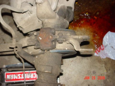 1978 Ford Bronco - A close-up view of a vehicle's suspension system, showing mechanical parts and a spill of red fluid on the ground.