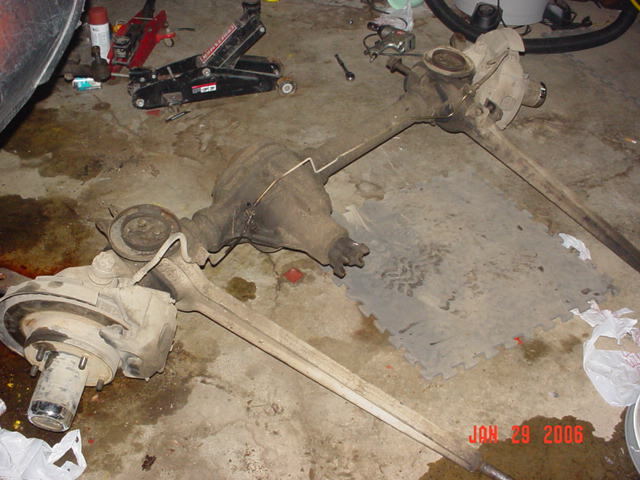 Two car axles and differentials on a concrete floor with a floor jack and tools in the background