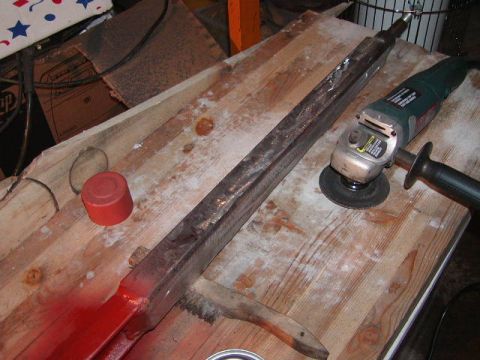 1978 Ford Bronco - A vehicle axle part is shown on a wooden workbench with an angle grinder and red paint, suggesting repair or modification.