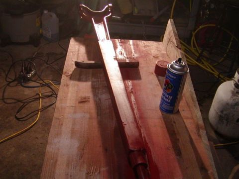 1978 Ford Bronco - A metal part is being painted red on a workbench with a can of spray paint nearby.