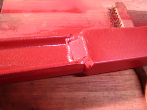 1978 Ford Bronco - A close-up view of a red painted metal component, possibly undergoing restoration or repair.