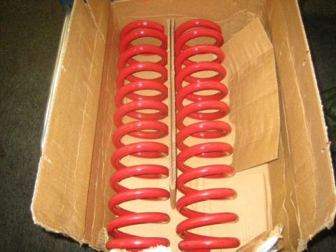 1978 Ford Bronco - Pair of red coil springs in a cardboard box, likely for vehicle suspension.