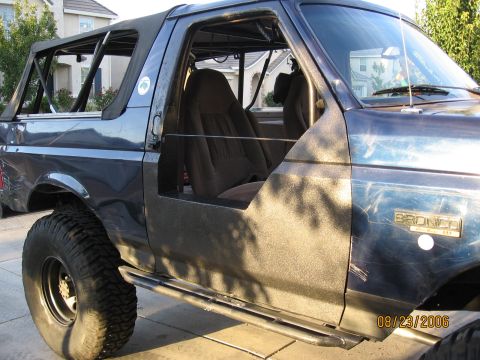 1994 Ford Bronco - Blue Ford Bronco with half doors removed, aftermarket roll cage, and large tires, seen from a 3/4 front angle.