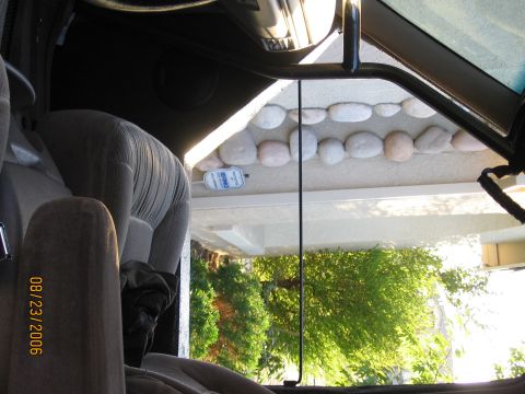 1994 Ford Bronco - Interior view of a vehicle, looking out through the window at a house and trees. A security sticker is visible on the exterior wall.