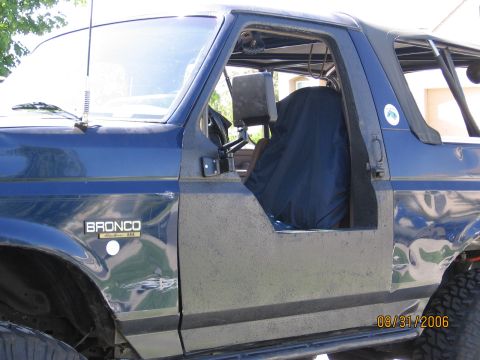 1994 Ford Bronco - A blue Ford Bronco is shown from the side, with the driver's door removed and the seat covered.