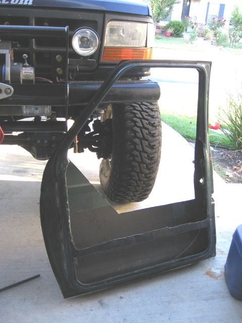 1994 Ford Bronco - A removed door lies next to the front of a 1992 Ford Bronco, revealing its winch and off-road tire.