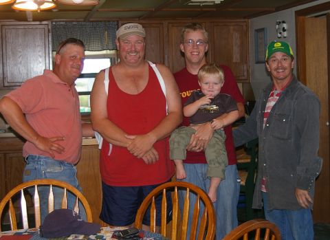 1998 Jeep TJ - A group of men and a child are gathered indoors, with one man wearing a distinctive green and yellow John Deere baseball cap.