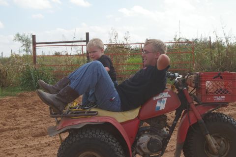 1998 Jeep TJ - Man and child ride on a red three-wheeled ATV in a dusty outdoor area.