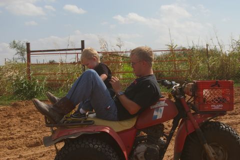 1998 Jeep TJ - A man and a young child sit on a red three-wheeled ATV in a dusty outdoor area.