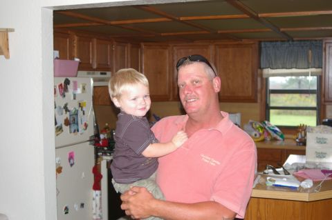 1998 Jeep TJ - A man holds a young child in a kitchen setting, with cabinets and a refrigerator visible in the background.