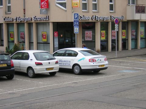1979 Ford Bronco - Two cars parked in front of a Caisse d'Epargne bank, one is marked as an ambulance.