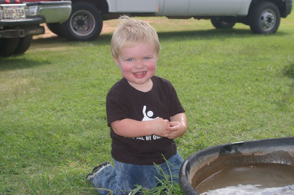 Child kneeling on grass in front of a white truck and a red truck