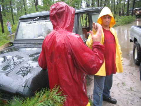 1990 Ford Bronco - People in rain gear stand near a vehicle stuck in the mud during a downpour.