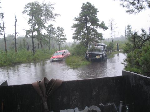 1990 Ford Bronco - Off-road vehicles navigate through a flooded path surrounded by trees.