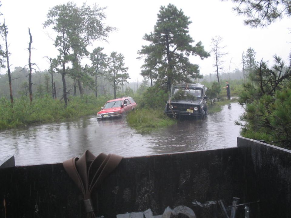 Two off-road vehicles are driving through a flooded wooded area. One is red, the other is black