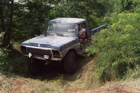 1979 Ford Bronco - Blue 1979 Ford Bronco navigating a dirt path surrounded by dense foliage.