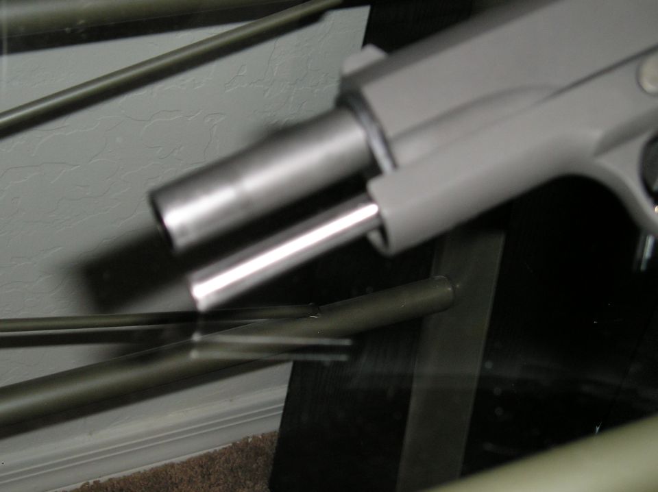 Blurry photo through cabinet glass of a stainless pistol and slender barrels