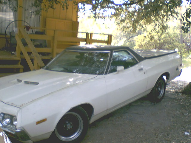 White 1972 Ford Ranchero parked outside a wooden structure with trees overhead