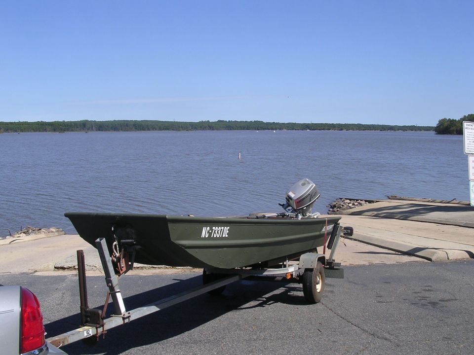 Green aluminum jon boat on a trailer at a lake ramp