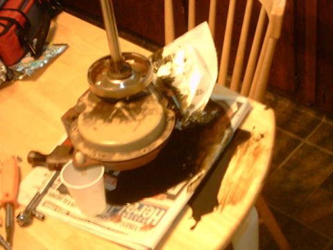 1979 Ford Bronco - An automotive part, possibly a carburetor or fuel pump, sits on a table atop a newspaper, with tools nearby.
