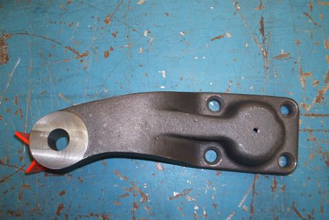 1983 Ford Bronco - A single metal steering arm part is shown against a blue, scratched surface. The part has a hole on one end and mounting holes on the other.