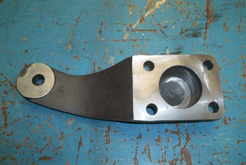 1983 Ford Bronco - A metal steering arm part is shown against a blue, textured surface. Text at the bottom reads 'SUPERMOTORS.NET'.