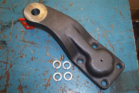 1983 Ford Bronco - A steering arm part is shown with accompanying washers and a grease fitting, laid out on a blue, textured surface.