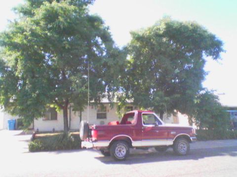 1990 Ford Bronco - Side view of a maroon full-size Ford SUV parked at the curb with its removable hardtop off, exposing the roll bar and red interior. It wear…